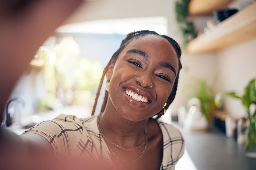 Smiling woman taking selfie in bright kitchen with plants visible